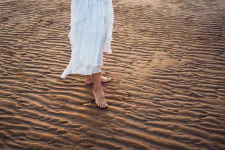 Girl in white dress walking on the beach at sunsetの写真素材
