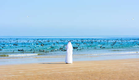 Arabic man photographing flock of birds in the sea