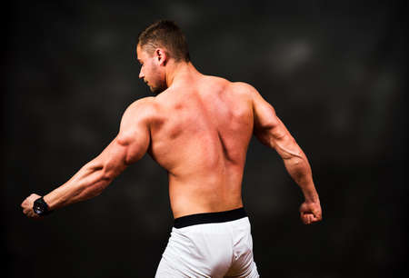 Bodybuilder flexing muscles against dark textured background