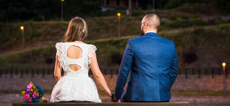 Bride and groom sitting by the lake at night