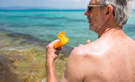 Senior man applying sun lotion on summer vacation back viewの写真素材