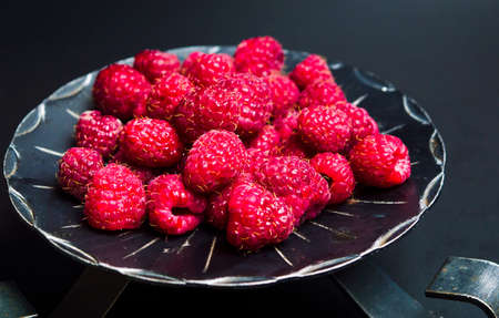Raspberry fruits on a dark bowl top view