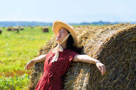 Asian girl relaxing outdoors in in a wheat field wearing red dressの写真素材