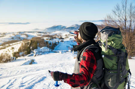 Man drinking from a hip flask on  snowy mountain topの写真素材
