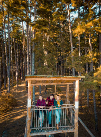 Two girls and a guy standing on the watchtower in the forest at autumn