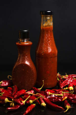Bunch of dried chilly peppers and bottles of red spicy sauceの写真素材
