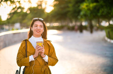Cheerful girl with cup of coffee walking outdoorsの写真素材