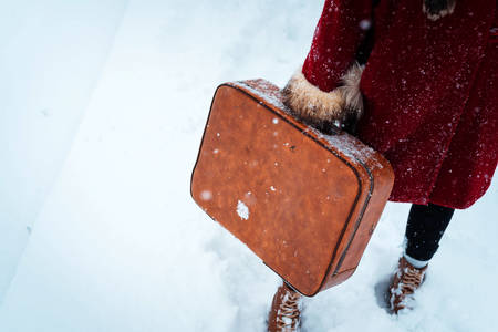 Girl in a red coat carrying an old suitcase in a snowstormの写真素材