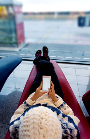 Girl using phone while waiting at the airport loungeの写真素材