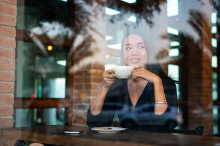 Woman having a cup of coffee by the window in the barの写真素材