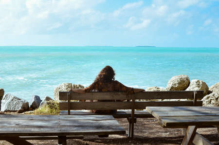Girl sitting on a bench next to the sea during summer