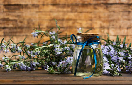 Rosemary oil in a bottle with flower branches on a tableの写真素材