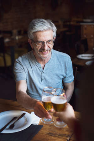 Senior man toasting with a beer in the barの写真素材