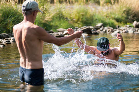 Father and son splashing each other with water in the river, summer funの写真素材