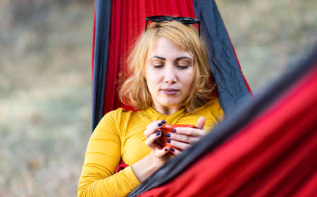 Woman sitting in a hammock with a cup of coffee in outdoorsの写真素材