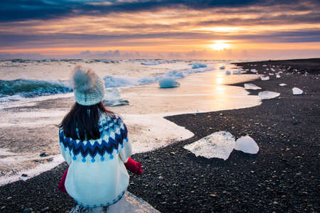 Woman sitting on iceberg and enjoying Diamond beach sunset in Icelandの写真素材