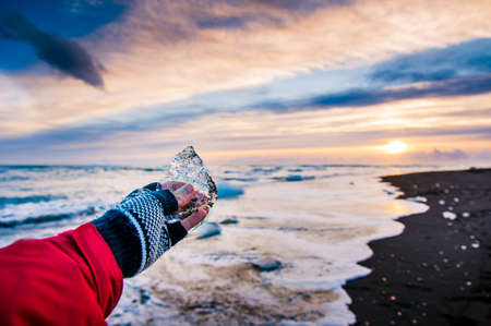 Traveler holding ice chunk on Diamond beach in Iceland during sunsetの写真素材