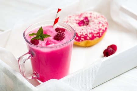 Raspberry smoothie in a decorated glass and a doughnut