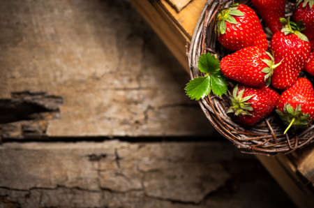 Strawberries in a wicker plate on a wooden tableの写真素材