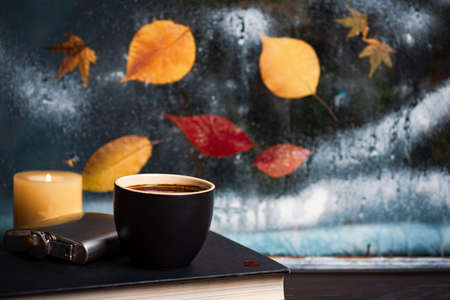 Cup of coffee and fallen autumn leaves on the window, cozy home athmosphereの写真素材