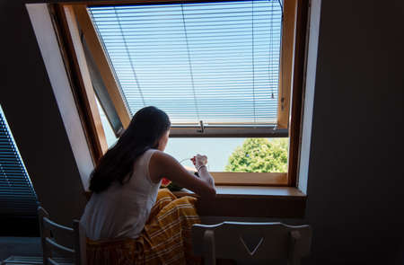 Young woman eating watermelon sitting by the window inside