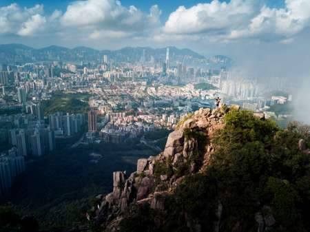 Man standing on the Lion rock above Hong Kong island under fog enjoying the view aerialの写真素材