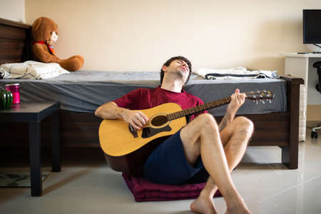 Man playing guitar in his bedroom and spending time at home practicing social distancingの写真素材