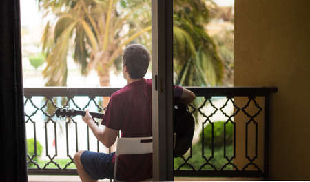 Man playing guitar on the balcony while spending time at home practicing social distancingの写真素材