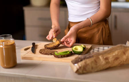 Woman making avocado peanut butter toast for a healthy breakfast at homeの写真素材