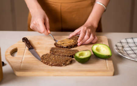 Woman making avocado peanut butter toast for a healthy breakfast at homeの写真素材
