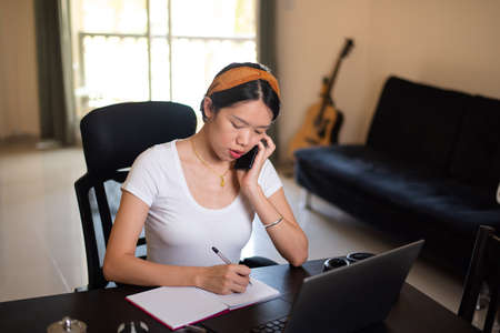 Busy woman on a phone meeting while working from home in an improvised office in the living roomの写真素材