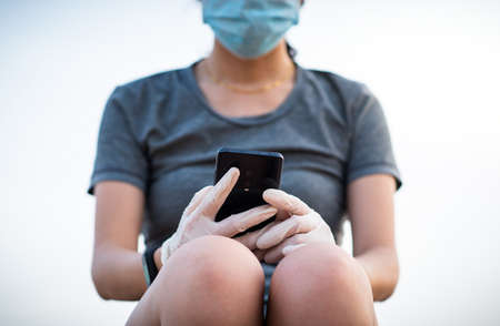 Woman using smart phone with protective gloves and mask