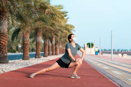 Asian woman exercising and stretching while wearing protective surgical mask to warm up before fitness workout outdoorsの写真素材