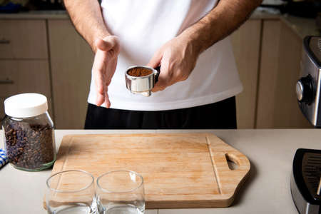 Man arranging coffee ground powder into portafilter basket. Home barista indoors lifestyle concept