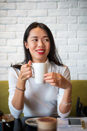 Asian woman having a cup of coffee in a bar closeup portraitの写真素材