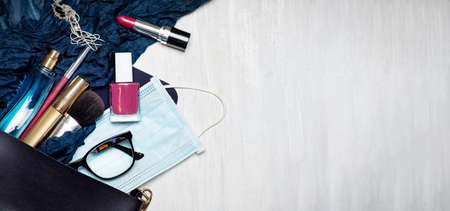 Surgical face mask with various makeup and cosmetic products falling out of an female bag tabletop...