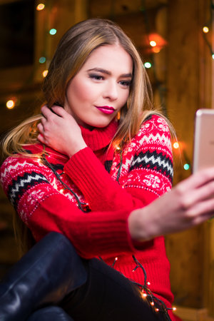 Girl taking a selfie wearing a festive red winter sweaterの写真素材
