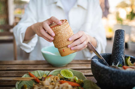 Woman opening sticky rice bamboo container while having a three course meal in a Thai restaurant closeupの写真素材