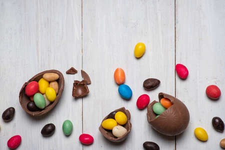Chocolate Easter eggs on a white wooden table with egg candies on a wooden table flat lay top view with copy spaceの写真素材