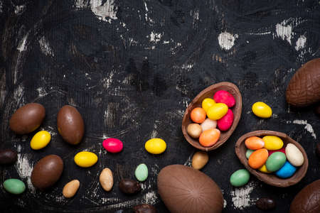 Chocolate Easter eggs on a dark wooden table with egg candies on a wooden table flat lay top view...
