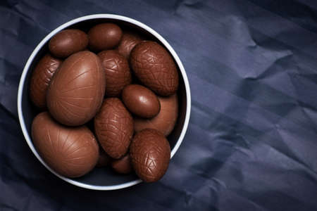 Chocolate Easter eggs with egg candies on dark paper background with copy spaceの写真素材