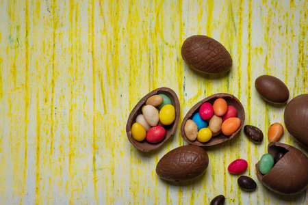 Chocolate Easter eggs on a yellow wooden table with egg candies on a wooden table flat lay top view with copy spaceの写真素材