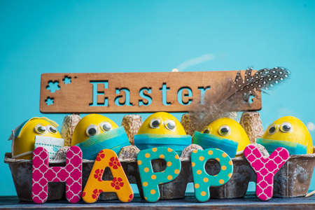 Happy Easter card with colorful hand Easter eggs wearing tiny surgical face masks on a colorful background with copy space.の写真素材