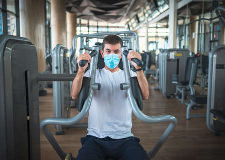 Man exercising in the gym on a pec deck machine for chest and pectoral muscles workout wearing surgical face maskの写真素材