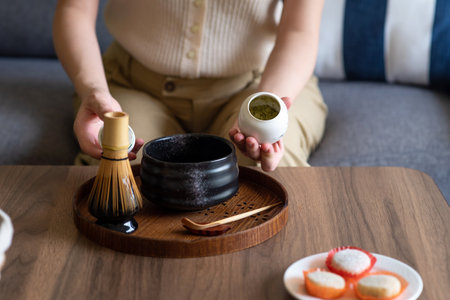 Woman making Japanese matcha green tea beverage at home using traditional tea ceremony bamboo set while sitting on the sofa at home.の写真素材