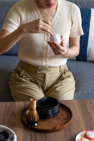 Woman making Japanese matcha green tea beverage at home using traditional tea ceremony bamboo set...
