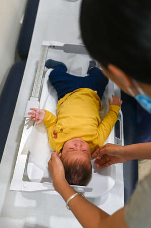 Doctor measuring length and weight of a 5 months old mixed race baby boy at the doctors office for a...