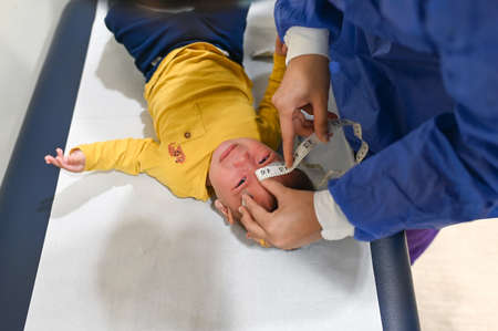 Doctor measuring crying 5 months old mixed race baby boy at the doctors office for a routine checkup...