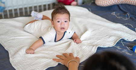 Mother playing with her 2 months old mixed race newborn baby boy lying on his tummy on the bed...