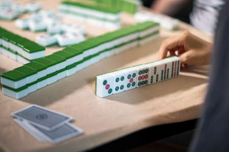 Female friends playing mahjong traditional Chinese board game at home. Translation: Tiles text shows Chinese characters for numbers from 1 to 9 and sides of the world: east, west, north,southの写真素材